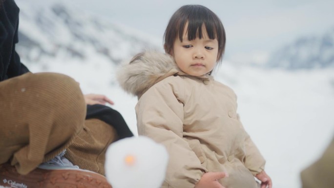 可爱的小女孩和她的家人坐在雪地上向上看。她看着弟弟堆雪人。