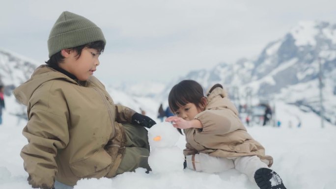 哥哥和姐姐一起坐在雪地上，谈笑风生，一起堆雪人，背景是美丽的山。