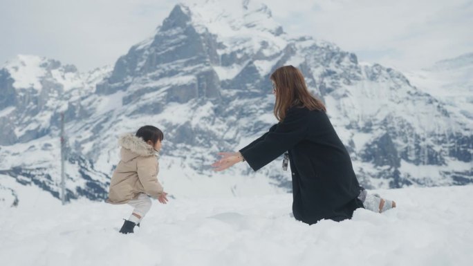 快乐的女婴试图站在雪地上，走着拥抱她的妈妈。