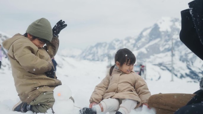 亚洲妈妈和她的孩子在雪中玩耍，一起把雪扔到空中。