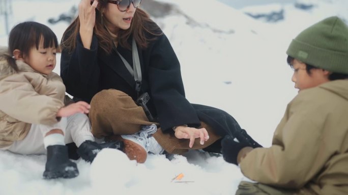 一群家庭坐在雪地上，一起玩雪人，在冬天的大自然中作为团队合作。