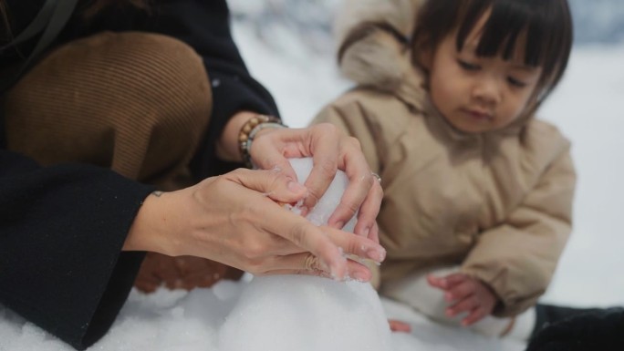 妈妈的手在冬天堆雪人，小女孩看着可爱的雪人。