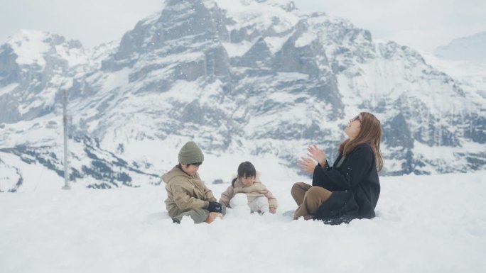 美丽的妈妈在雪地里和小男孩小女孩玩，还把雪抛向空中。