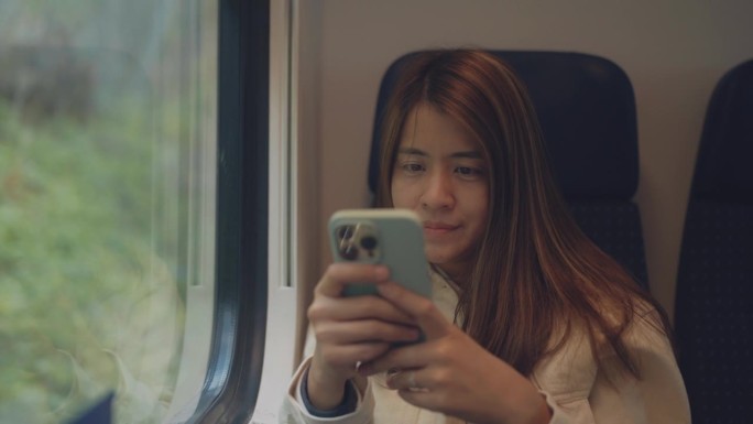 快乐的亚洲女性在火车上用智能手机看直播，用手机玩社交媒体。