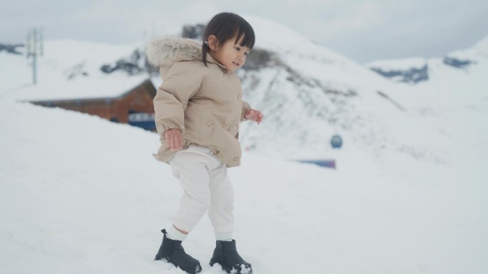 快乐的小女孩站在雪地上走着。她穿着暖和的衣服在山上玩。