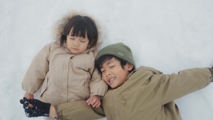 可爱的小男孩和小女孩躺在雪地里看着镜头。