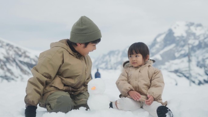 哥哥和姐姐一起坐在雪地上，谈笑风生，背景是山。