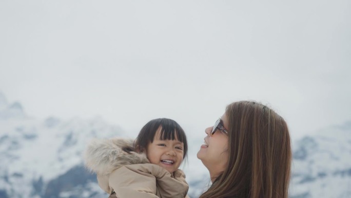 快乐的亚洲妈妈抱着可爱的女孩，在度假的雪山一起玩耍。