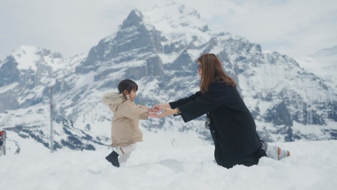 快乐的女婴让她踩在雪地上，走着拥抱她的妈妈。