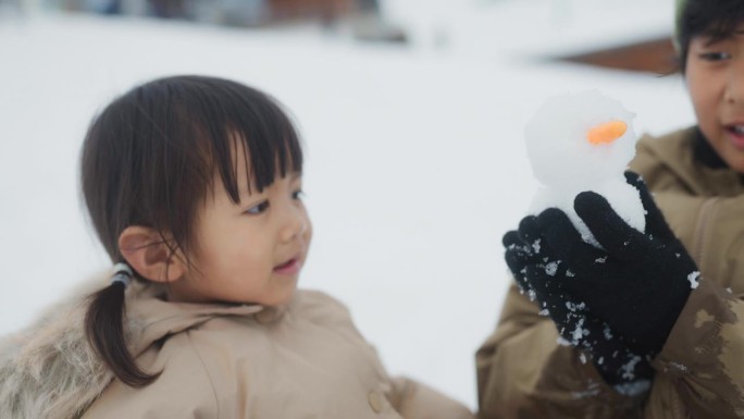 度假时，小男孩在雪地公园为他的小妹妹堆了一个可爱的雪人。