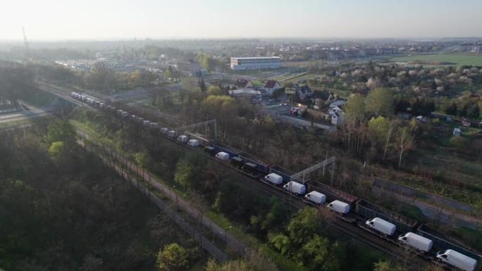一架无人机拍摄到两列货运列车在早上穿过城市，其中一列载着空车，另一列载着新的运货货车。他们穿过高架桥