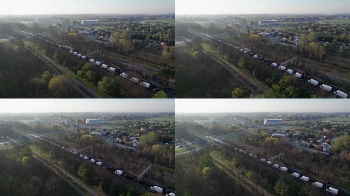 一架无人机拍摄到两列货运列车在早上穿过城市，其中一列载着空车，另一列载着新的运货货车。他们穿过高架桥