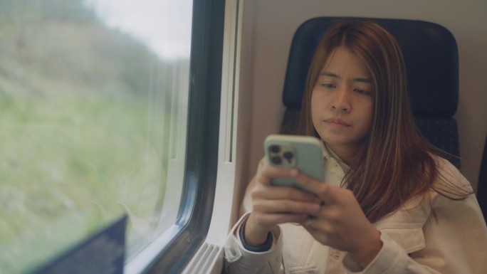 一名亚洲妇女在火车上旅行，并在火车上查找信息查看旅行计划。
