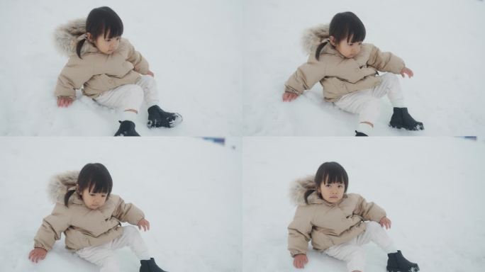 女婴穿着暖暖的冬衣，兴奋地坐在雪地上，动来动去。