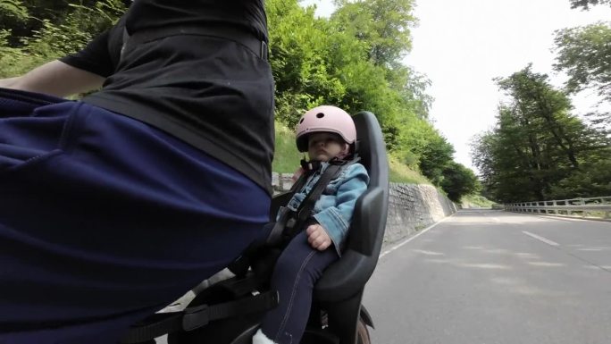 宝宝坐在自行车后座的婴儿座椅上，骑在宁静的乡间小路上，穿越大自然