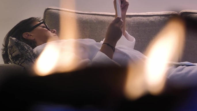 一个女人躺在豪华房间里壁炉后面的沙发上看报纸