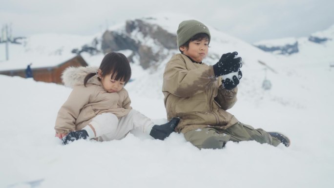 男孩和女孩一起坐在雪山上，哥哥给妹妹堆了一个可爱的雪人。