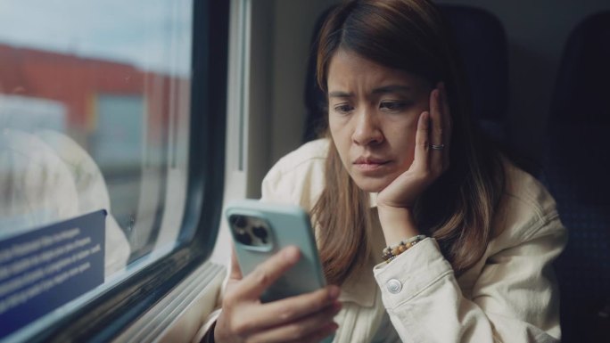 亚洲女商务人士在行驶的火车上阅读手机短信。