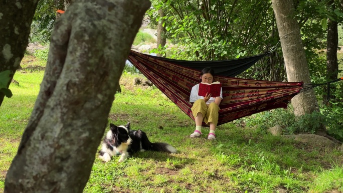 坐在河边树林里吊床上读书的女生，和她的狗