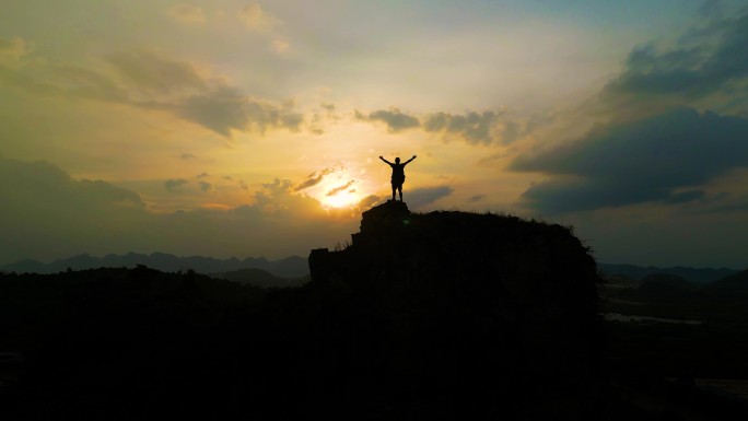 登山行者站在山顶张开双臂拥抱太阳眺望远方