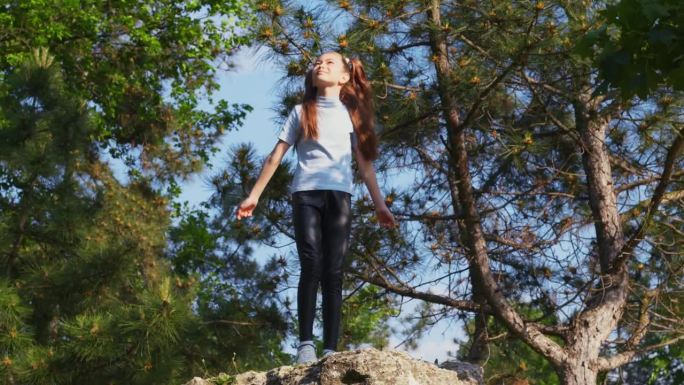 小女孩站在森林中央的一块石头上，举起双臂