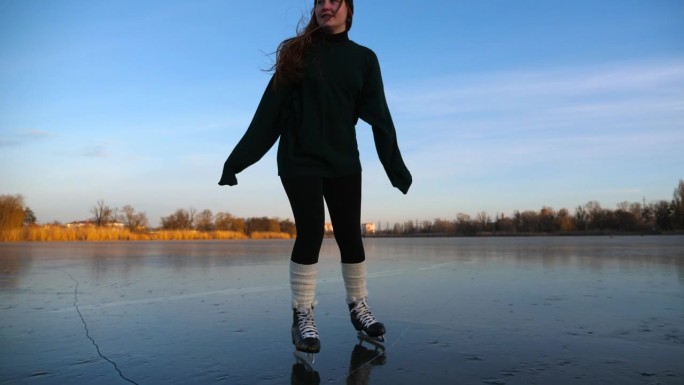 穿着花样滑冰鞋微笑着的年轻女子在冰上滑行。快乐的女孩在结冰的河上滑冰。女运动员在冬天寒冷的日子里享受