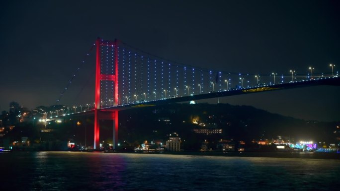 土耳其伊斯坦布尔，博斯普鲁斯大桥的夜景。从一艘漂浮的船上望去，灯火通明，桥上移动着汽车