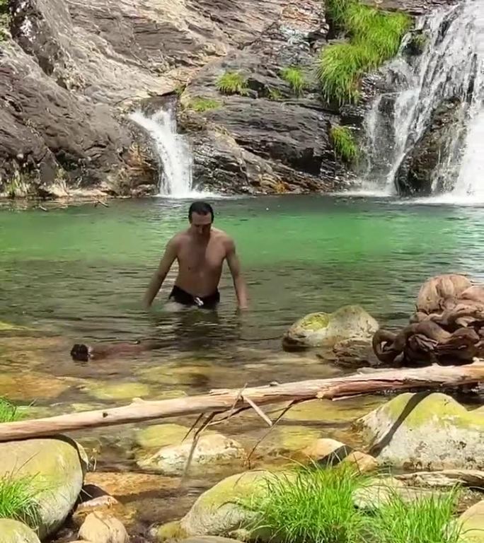 像泰山一样英俊性感的黑发男人从瀑布附近的山河中走出来，就像冒险电影里的镜头一样