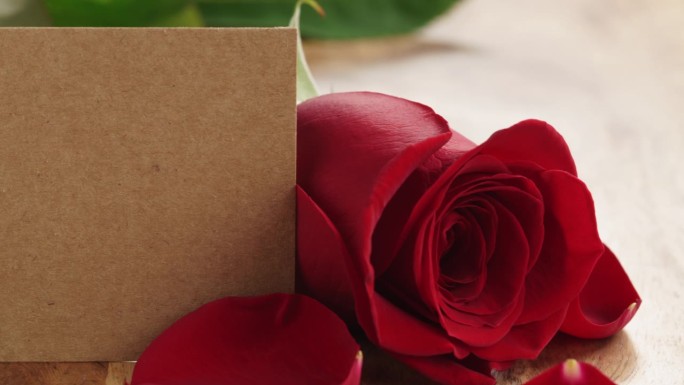 特写一盘美丽的红玫瑰与花瓣和空纸卡在旧木桌