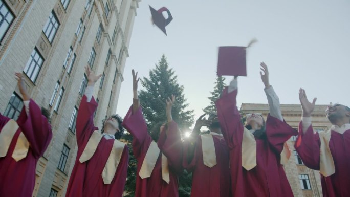 在大学校园里，穿着长袍、向天空抛帽子的快乐男女庆祝毕业