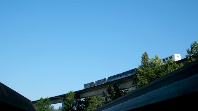 天空列车从下至上的蓝线列车通过天空天桥的背景在新威斯敏斯特弗雷泽河拖船，新威斯敏斯特天际线。一艘拖船