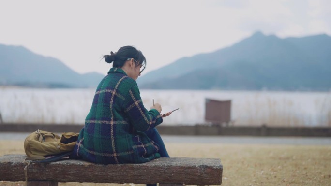 坐在湖边的女人她用平板电脑画美丽的风景作为她的内容。她是一个旅游博主