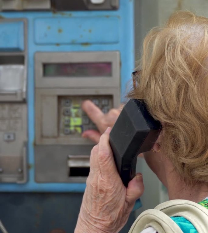 老妇人在一个旧电话亭里拨打电话