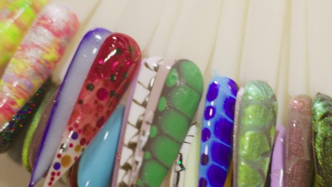 美甲师向客户展示五颜六色的塑料针尖和个性化设计的指甲。大师使用从丙烯酸凝胶提示。不同的设计，色彩斑斓