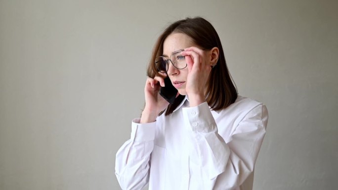 一位穿着白衬衫、戴着眼镜、神情严肃的年轻女子正在讲电话