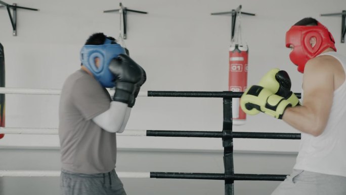 两个年轻的拳击运动员戴着头盔和手套在体育馆里进行拳击训练
