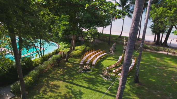 空中无人机俯瞰婚礼拱门和海滩附近花园的椅子。在绿色草坪上装饰的婚礼。晴朗的夏天。美丽的婚礼装饰在夏日