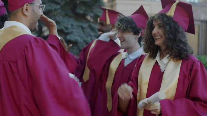 一群学生身穿毕业礼服，头戴毕业帽，手持毕业证书，在校园里击掌致意