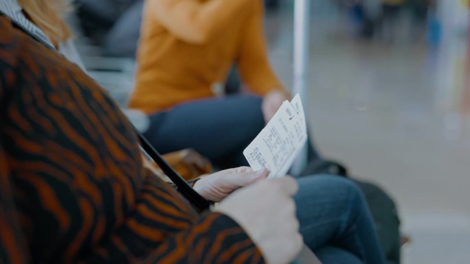 两位女性朋友坐在机场登机口检查登机牌