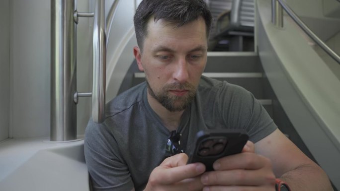 年轻人乘坐双层火车，坐在飞机上玩智能手机。火车旅行期间没有座位。男性乘坐双层火车上下班，坐在飞机上上