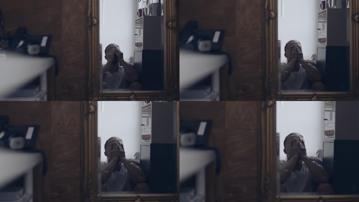 一个忧郁的男人独自坐在镜子里。双手掩面
