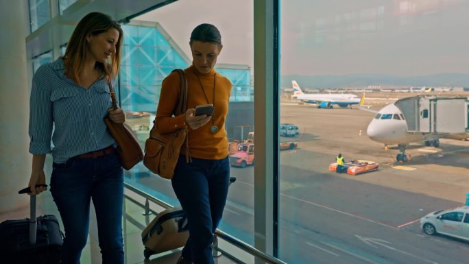 女士和朋友在机场门口散步时查看智能手机