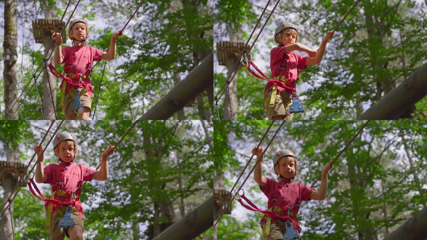 一个小男孩正在郁郁葱葱的森林里享受一场惊险刺激的绳索障碍赛。他戴着头盔，系着安全带，在充满挑战的赛道