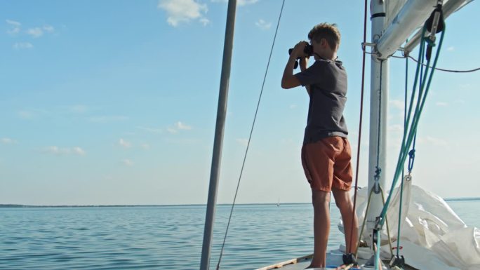 十几岁的男孩在游艇上通过双筒望远镜观看
