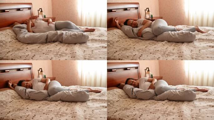 迷人的孕妇采用舒适的睡姿，使用特殊的肚子支撑枕头