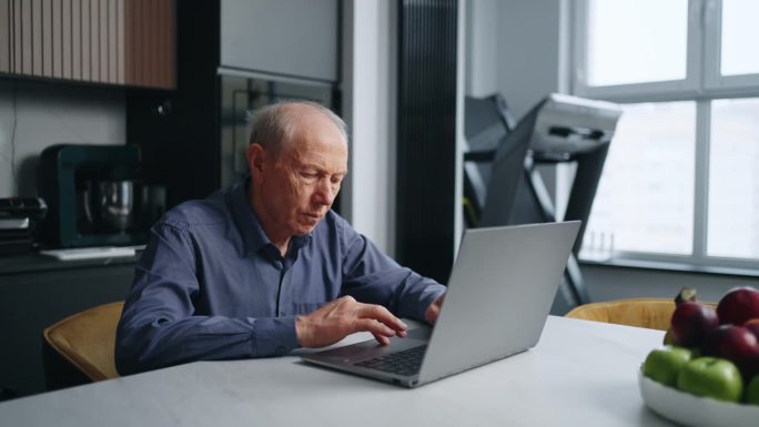 老年男子在厨房用笔记本电脑工作，老年男子上网的肖像