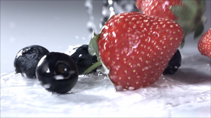 蓝莓和草莓在白色背景上滚下来。慢动作
