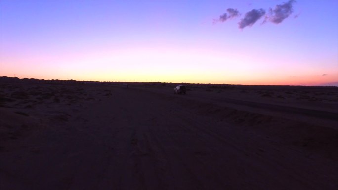 航拍黎明沙漠公路上迎着朝霞行驶的吉普车