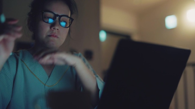 年轻、困惑、沮丧的亚洲女商人在深夜阅读笔记本电脑屏幕上的信息。