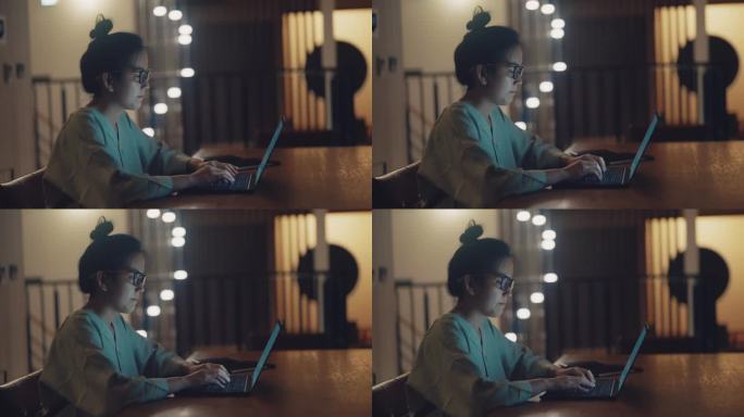 年轻的亚洲女性晚上坐在家里客厅的办公桌前用笔记本电脑工作。